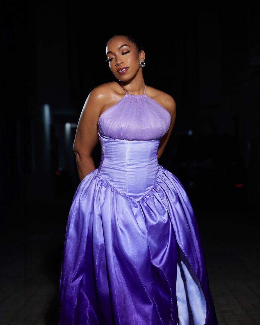 Eki Ogunbor in a lilac corseted gown, eyes closed, against a dark background